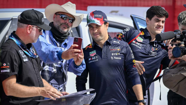 Checo Pérez mira la pantalla de un celular de un señor con lentes