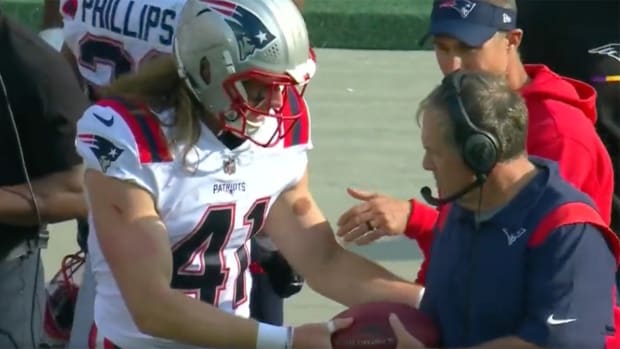 Patriots rookie hands a football to coach Bill Belichick.
