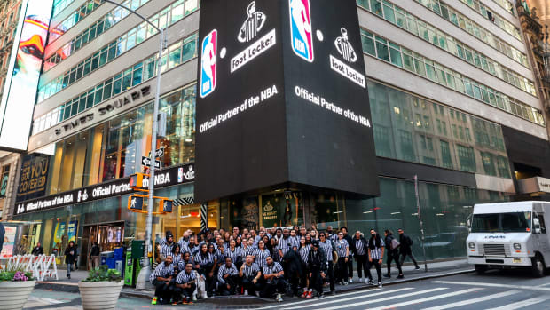 Foot Locker employees pose for a picture beside an NBA billboard.