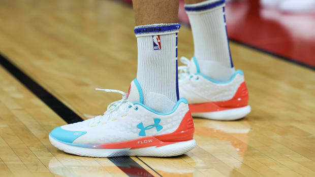 View of white, teal, and orange Under Armour shoes.