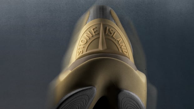 View of a gold Stone Island logo on the back of a New Balance running shoe.