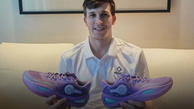 Austin Reaves holds purple and teal Rigorer sneakers.