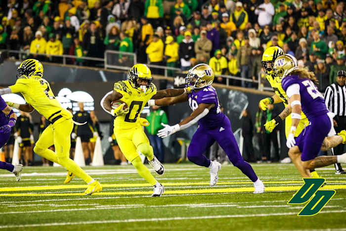 Oregon Ducks running back Bucky Irving stiff arms a Washington Huskies defender.