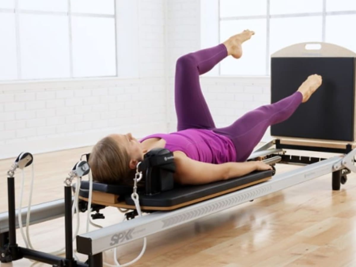 Male athlete with hands behind head practicing pilates on cadillac