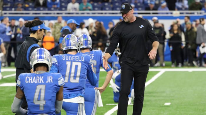 Lions coach Dan Campbell reaches out to shake players' hands as they stretch before a game.