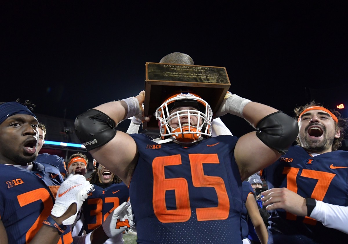 Nov 27, 2021; Champaign, Illinois, USA; Illinois Fighting Illini offensive lineman Doug Kramer (65) lifts the Land of Lincoln trophy after defeating the Northwestern Wildcats at Memorial Stadium. Mandatory Credit: Ron Johnson-USA TODAY Sports