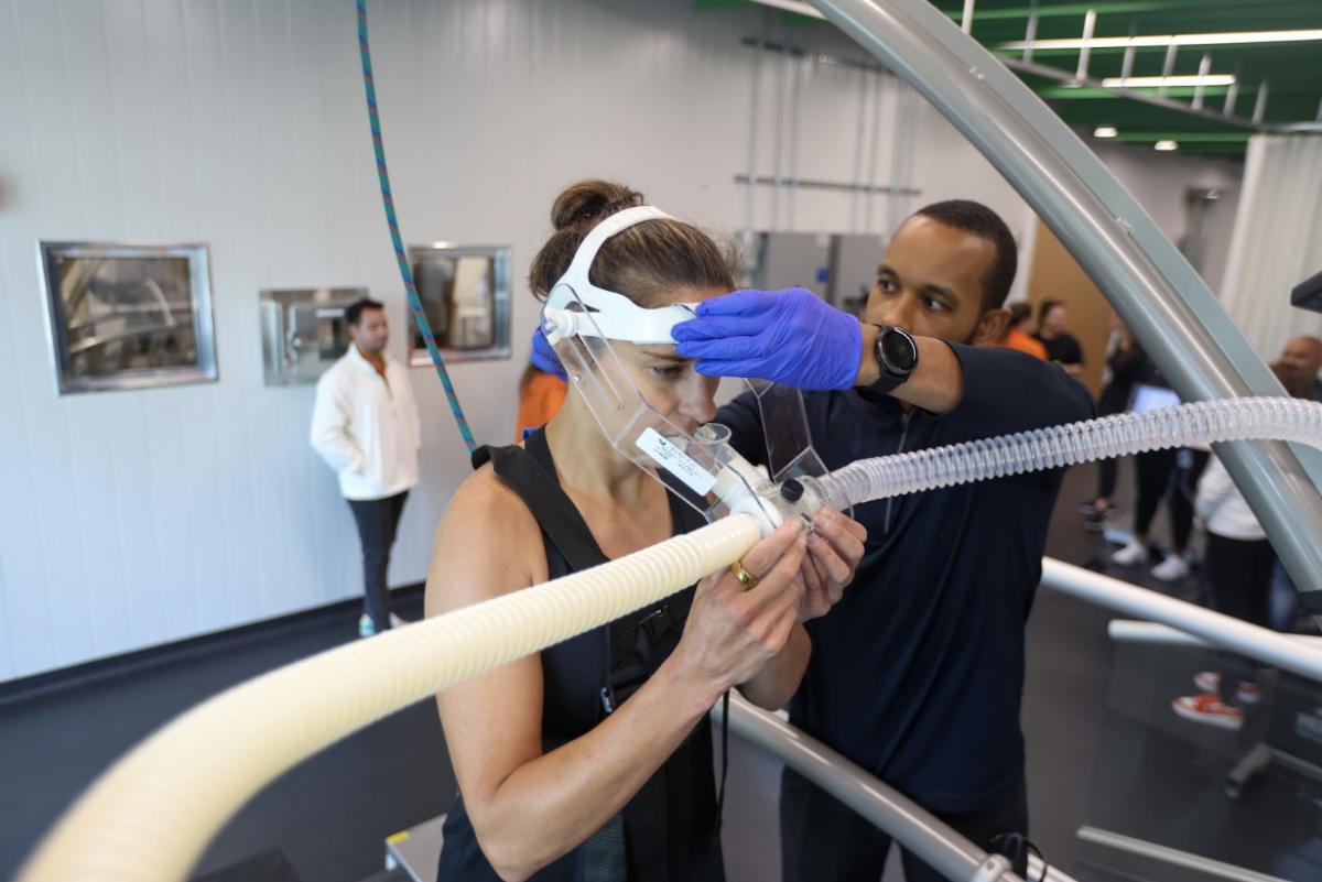 Carli Lloyd stands with a device connected to tubes as a man attaches it to her head