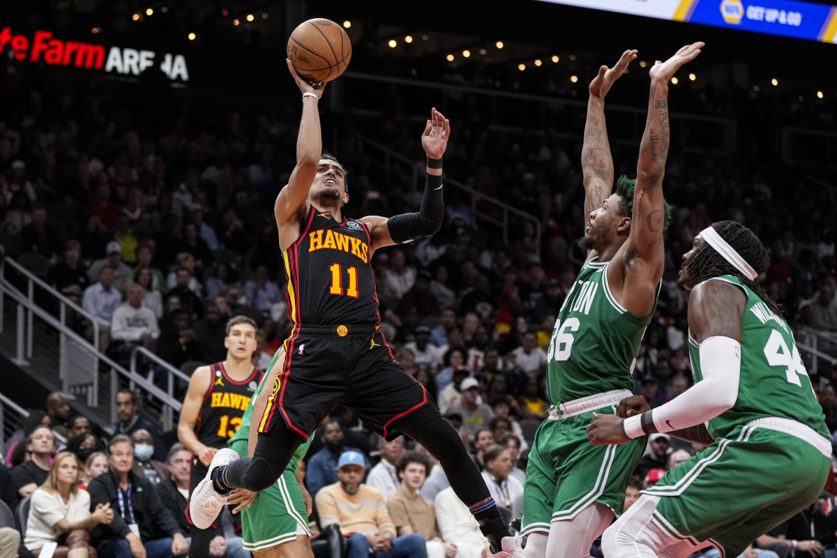 Trae Young jumps shooting the ball as two Celtics defenders stand in front of him