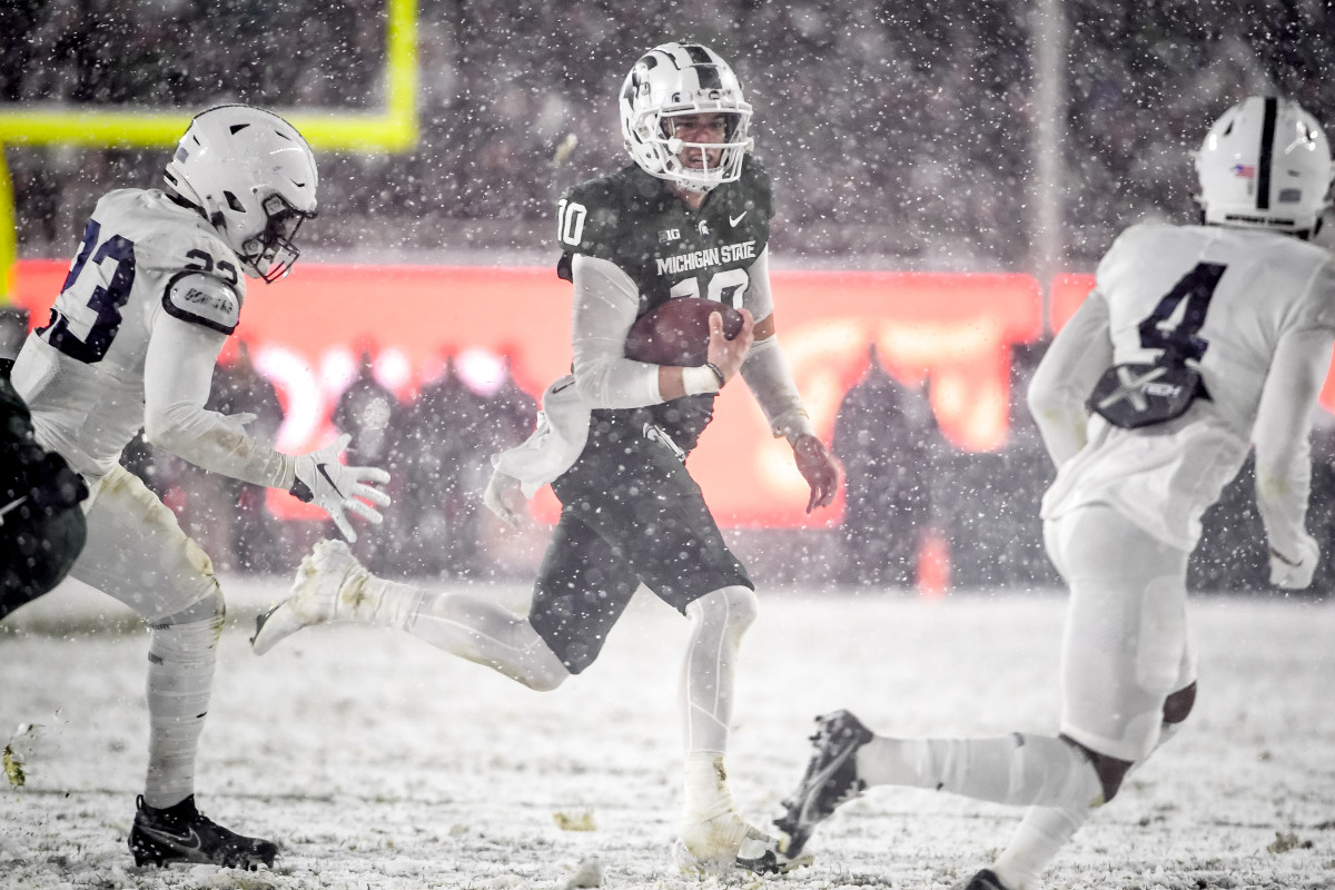 EAST LANSING, MICHIGAN - NOVEMBER 27: Payton Thorne #10 of the Michigan State Spartans runs the ball against Curtis Jacobs #23 and Kalen King #4 of the Penn State Nittany Lions during the fourth quarter at Spartan Stadium on November 27, 2021 in East Lansing, Michigan. (Photo by Nic Antaya/Getty Images)