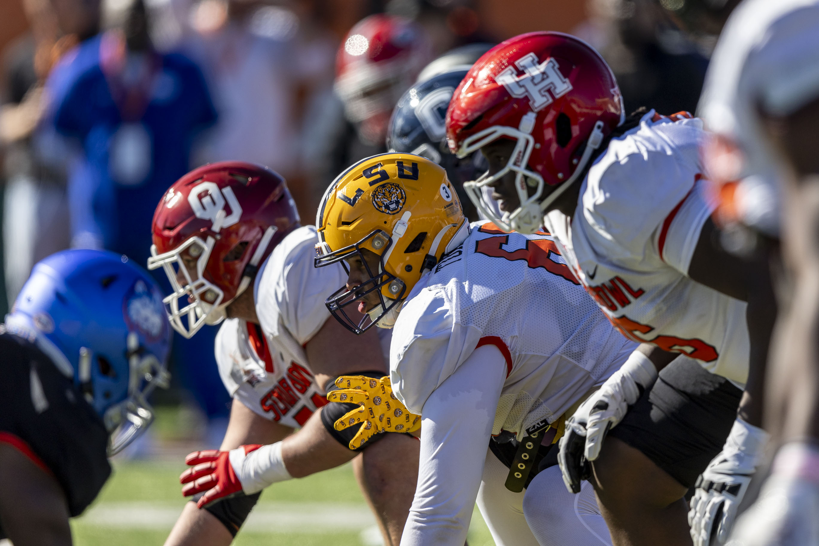 Various linemen bend over to prepare for the snap, with OU, LSU and UH on their helmets