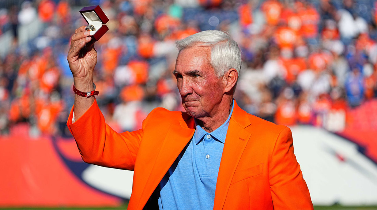 Mike Shanahan wearing an orange jacket being inducted into the Broncos Ring of Fame