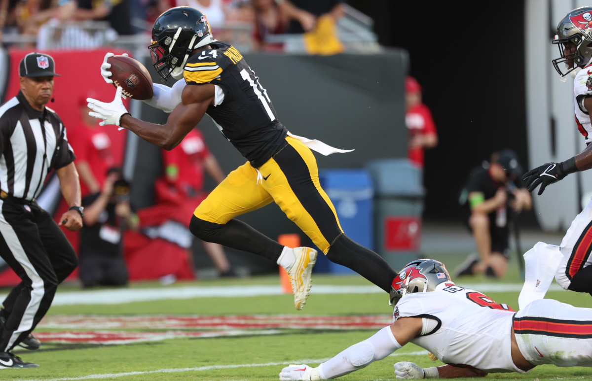 George Pickens holds the ball with one hand, sprinting with one leg up to try for a touchdown