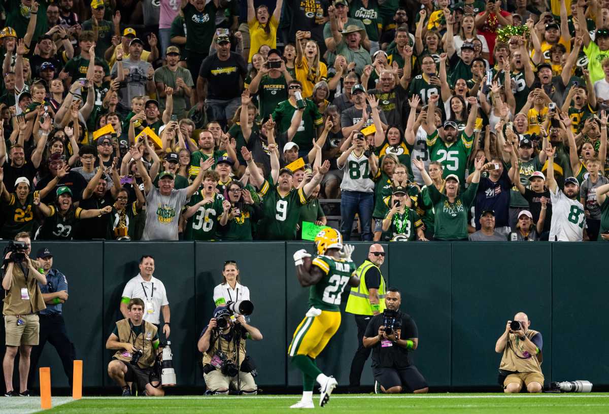 A Packers player runs with the ball in his hands as the crowd in the stadium stands up and cheers