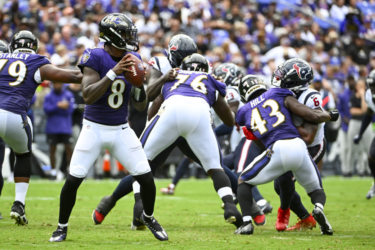 Lamar Jackson holds the ball in both hands preparing to throw as his O-line blocks Texans players to his side