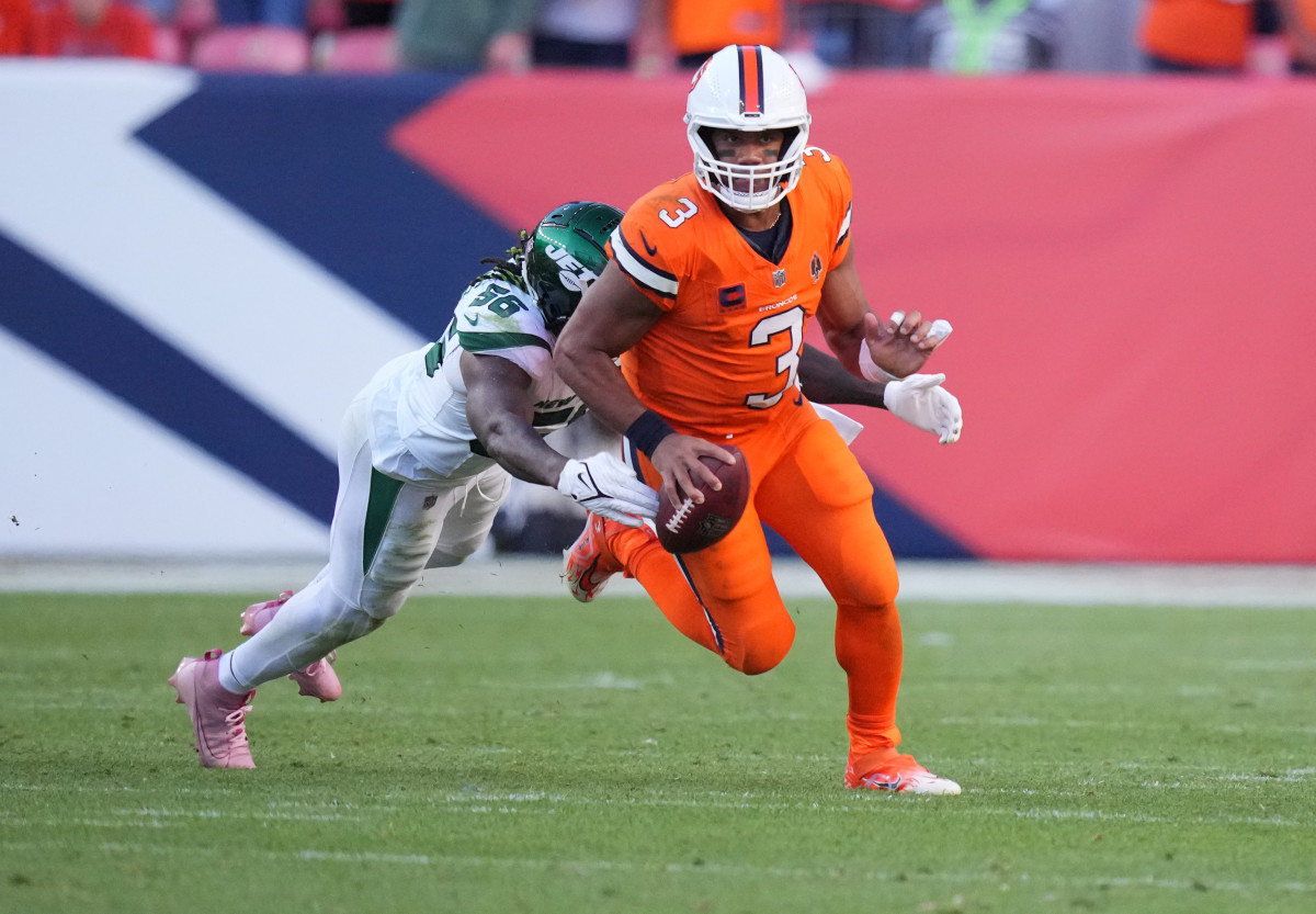 Russell Wilson runs with the ball in one hand while a Jets defender lunges to tackle him