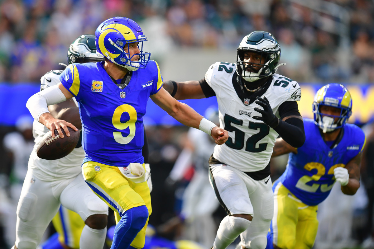 Matthew Stafford holds the ball in one hand looking to throw as an Eagles defender runs toward him