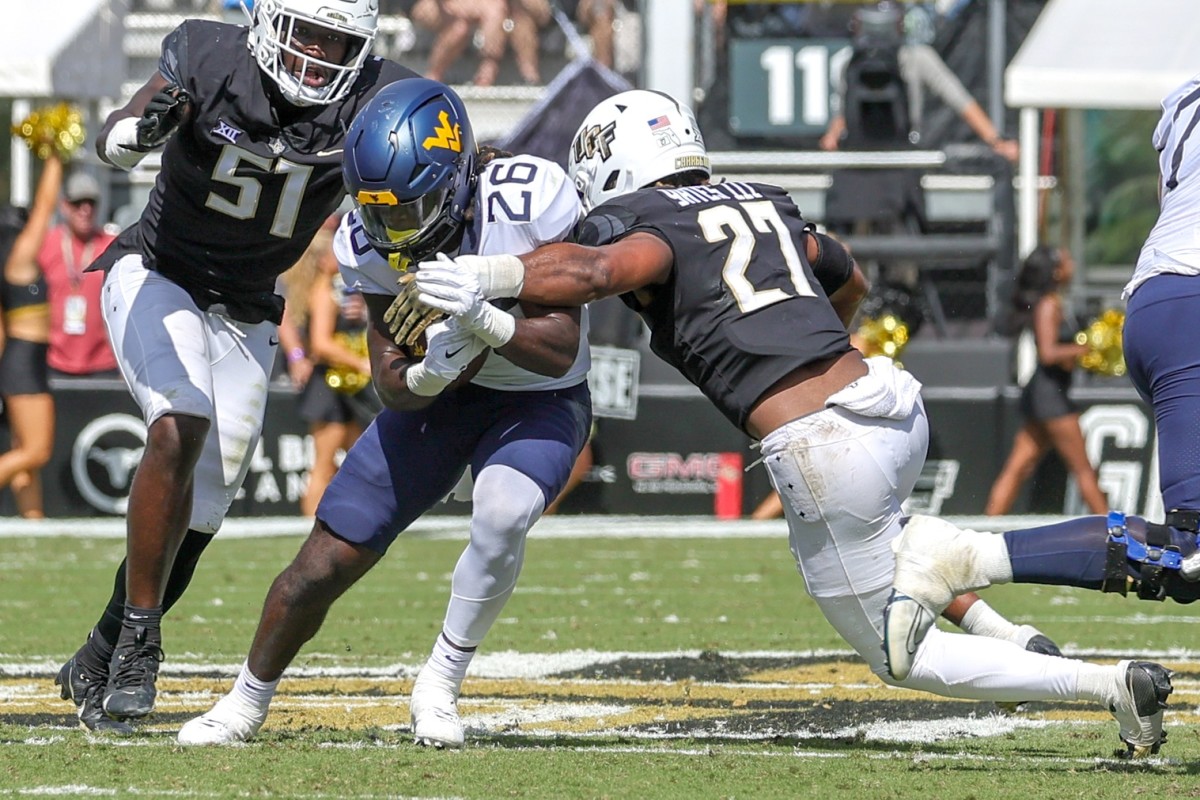 Oct 28, 2023; Orlando, Florida, USA; West Virginia Mountaineers running back Justin Johnson Jr. (26) is tackled by UCF Knights linebacker Walter Yates III (27) during the second quarter at FBC Mortgage Stadium.