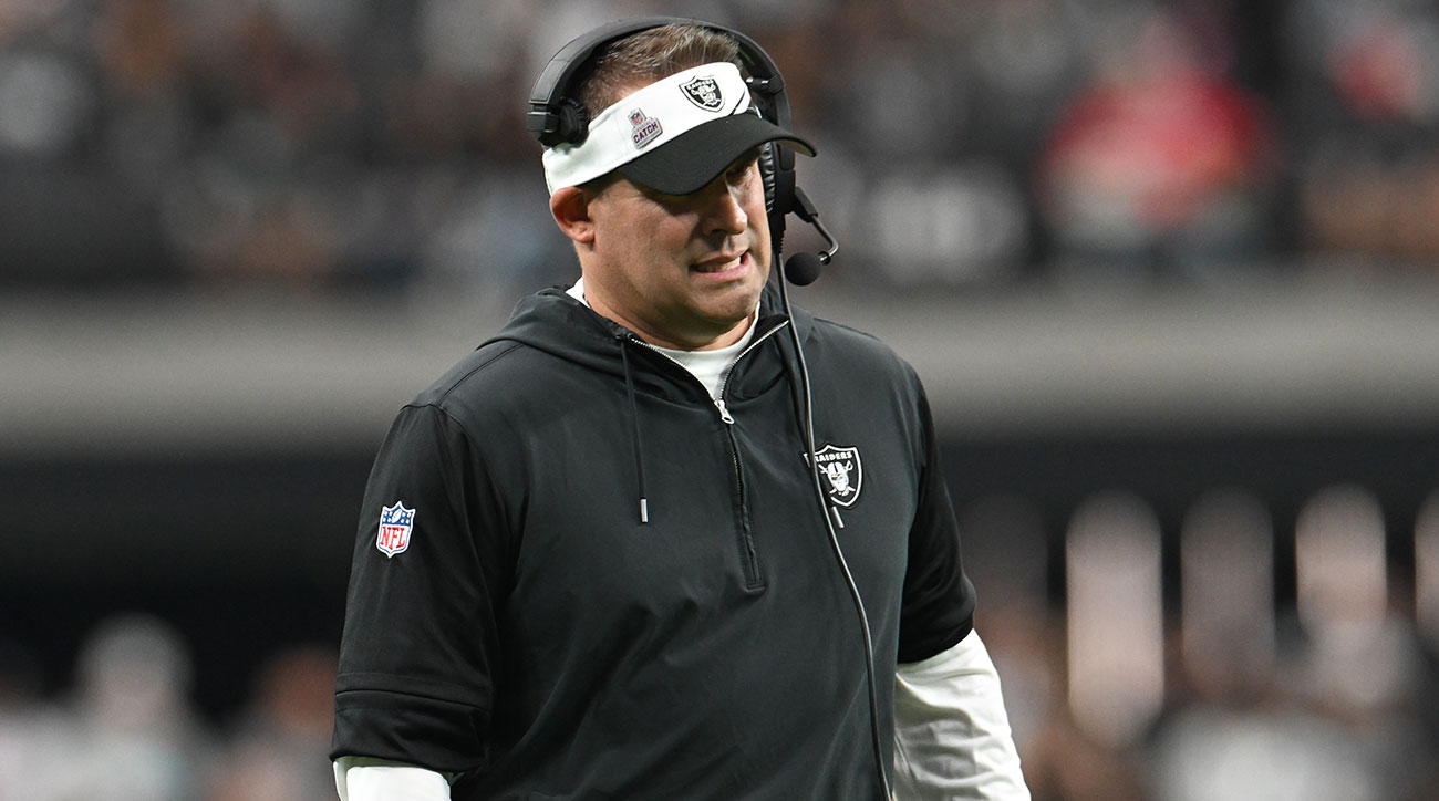 Josh McDaniels grimaces as he looks out on the field wearing a visor.