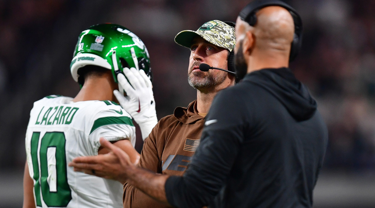 Aaron Rodgers looks up wearing a headset as robert saleh stands next to him talking and gesturing with his left hand