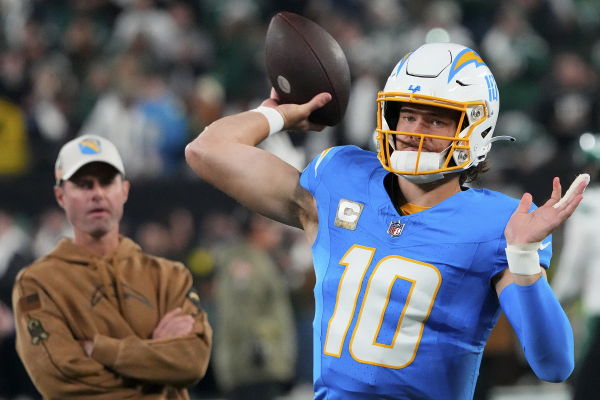 Justin herbert throws while Brandon Staley watches from behind him