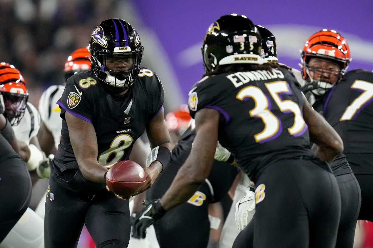 Lamar Jackson reaches to pass the ball off to a Ravens running back as Gus Edwards runs up to him