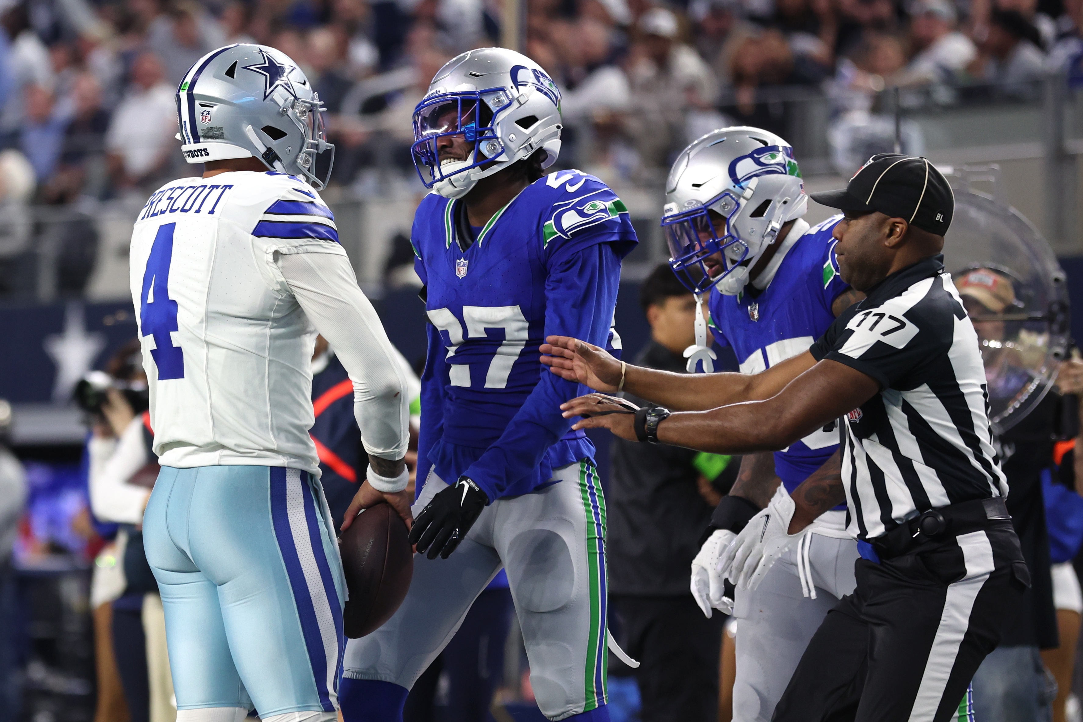 A referee attempts to break up Cowboys quarterback Dak Prescott and Seahawks cornerback Tariq Woolen.
