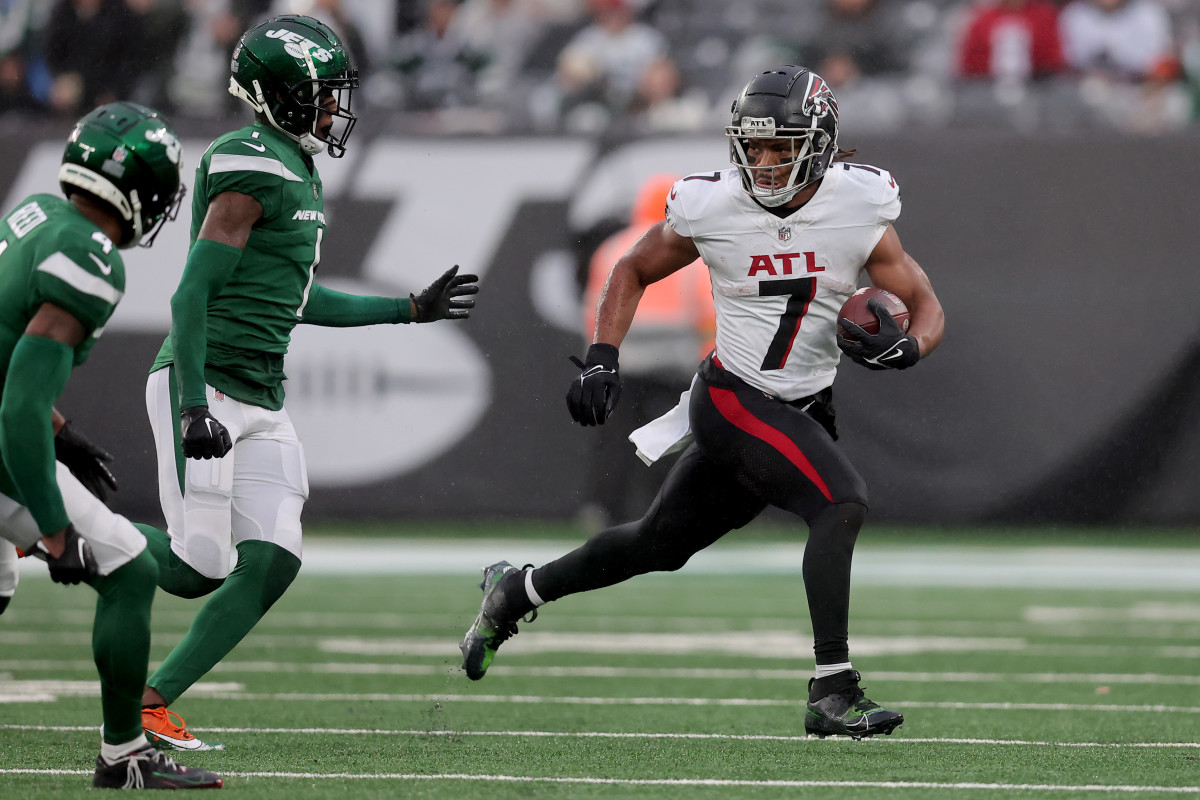 Bijan Robinson runs with the ball in one hand as two Jets players approach him