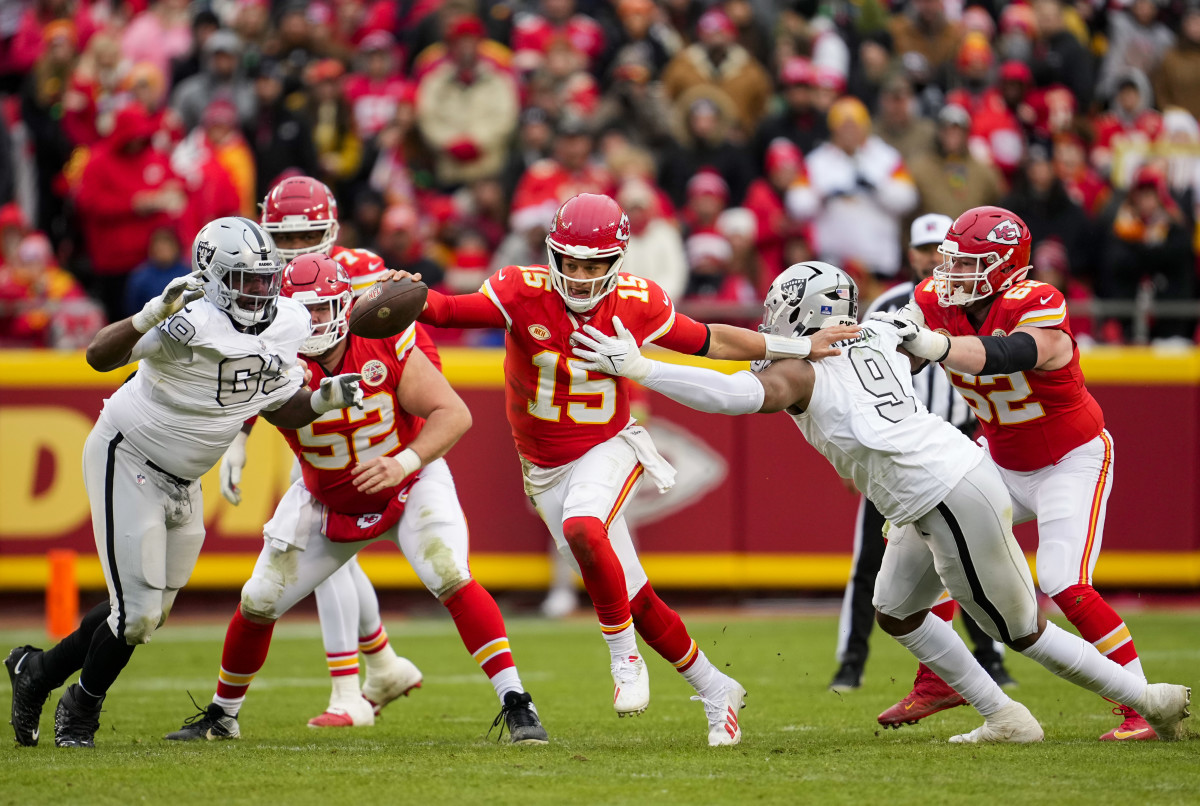 Patrick Mahomes runs with the ball outstretched in one hand as Raiders players try to tackle him