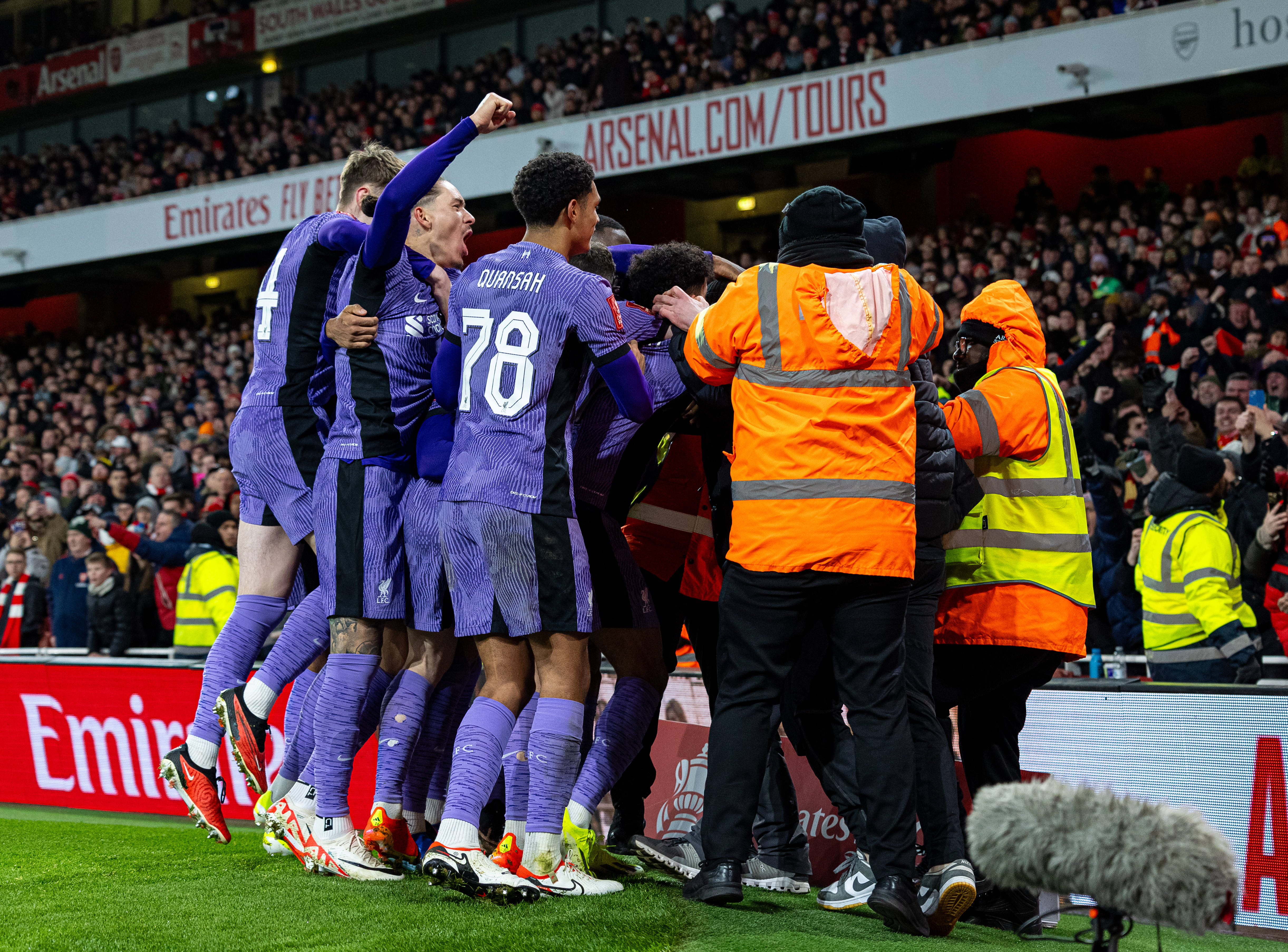 Liverpool's players pictured celebrating a goal during a 2-0 win at Arsenal in January 2024 while security staff at the Emirates Stadium attempt to remove a pitch invader from the field