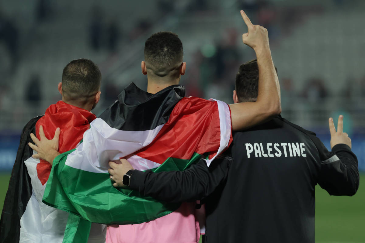 Two Palestine players and a member of coaching staff pictured celebrating after a 3-0 win over Hong Kong at the AFC Asian Cup in January 2024