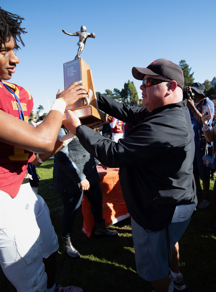 Coach Phil Ferrigno (right) holds the trophy with one of his players following Lincoln's 35-0 win over Balboa for the San Francisco Section title at Kezar Stadium. 