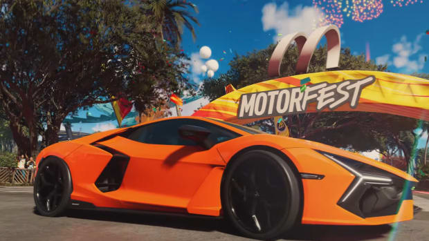 The Crew Motorfest preview: An orange sports car is drifting hard while turning left in front of a yellow arch with 'Motorfest' written on it