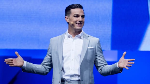 EA CEO Andrew Wilson, standing in front of a blue screen with his hands spread apart