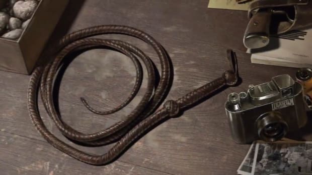 A whip, camera, and revolver on a desk.