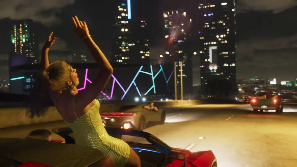 A woman in a tight-fitting yellow dress is standing in a car with her hands up as it speeds down a highway